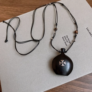 Detail of gothic black resin bottle necklace with silver cross on woven rope cord