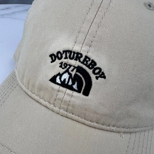Gros plan sur la broderie noire 3D et le logo de montagne sur une casquette en coton beige