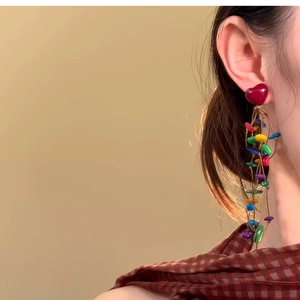 Close-up of a model wearing colorful beaded heart tassel earrings with silver needle