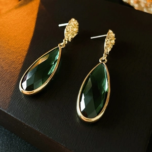 Detail of vintage emerald teardrop earrings with textured gold accents on a wood stand