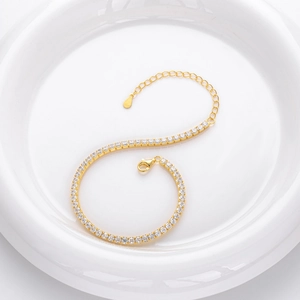 Detailed shot of an S-shaped gold tennis bracelet with zircons on a white plate
