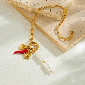 Bracciale dorato con perle, stella marina e peperoncino su una base di pietra beige