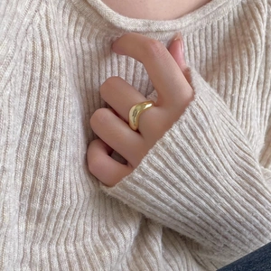 Close-up of a thick curved gold ring worn on a finger with a cozy knit sweater background