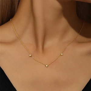 Close-up of three gold star pendants with white stones on a delicate silver necklace