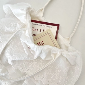 Dettaglio della borsa tote in cotone bianco con ricamo floreale in pizzo e bordi a volant