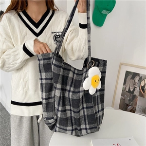 Close-up detail shot of a large plaid woolen tote bag being carried by a young woman