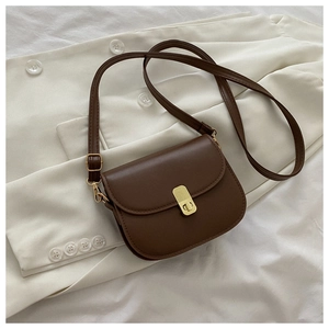 Detailed view of a dark brown matte leather saddle bag with gold buckle on a white blazer