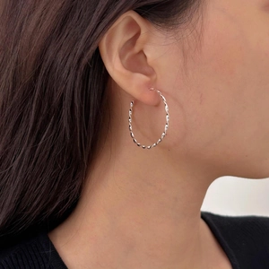 Close-up of a silver twisted rope hoop earring worn by a model for a stylish daily look