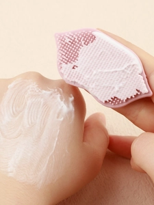 Detailed view of pink silicone facial brush massaging foam on hand for deep pore cleansing