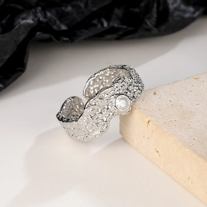 Detailed close-up of a silver textured ring with clear gemstone on beige stone