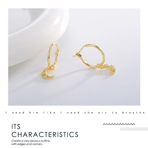 Detailed close-up of gold moon dangle earrings with micro-set zircon stones on white ceramic