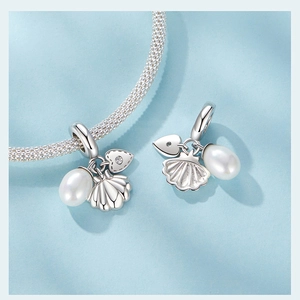 Détail macro de breloques en argent S925 coquillage, perle et cœur sur bracelet