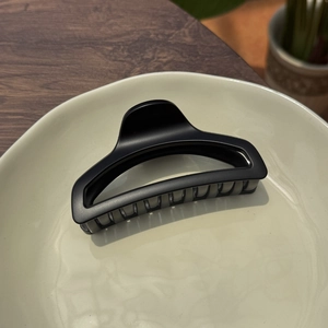 Close-up of matte black 10cm perfume bottle hair claw clip on a ceramic tray