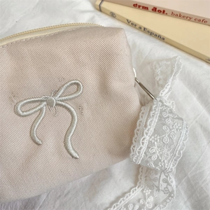 Close-up of beige canvas makeup bag with 3D bow embroidery and delicate lace ribbon