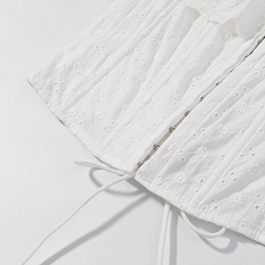 Dettaglio della camicetta in cotone bianco ricamato con ganci metallici e laccio in vita