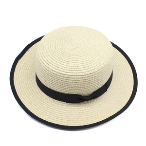 Detail view of the flat top straw hat featuring a black bow ribbon and contrast piping
