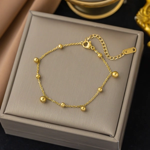 Minimalist gold beaded stainless steel chain bracelet on a luxury gray jewelry box