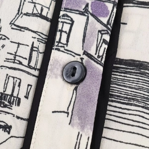 Close-up of violet printed fabric with fine stitching and a black round button detail