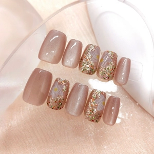 Detail of nude pink cat-eye press-on nails with daisy floral art and glitter sequins