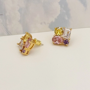 Detailed close-up of geometric gold earrings with colorful zircon stones and secure backs