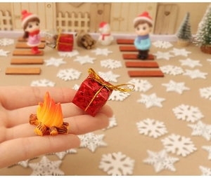 Detailed close-up of miniature Christmas campfire model and red gift box held by hand