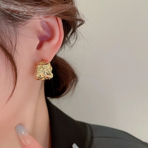 Detailed close-up of a model wearing the irregular pleated gold metallic C-shape earrings