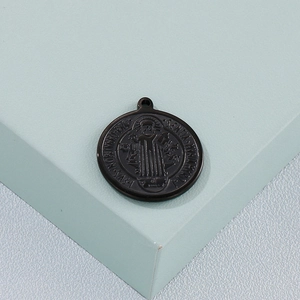 Detailed close-up of a black circular metal pendant with St. Benedict relief engraving