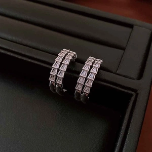 Detail of silver C-shaped earrings with rectangular cubic zirconia on black tray
