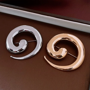 Detailed view of snail spiral brooches in polished gold and silver on leather background