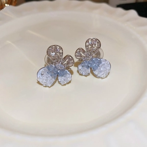 Macro view of blue crystal butterfly stud earrings with silver needle on white ceramic plate