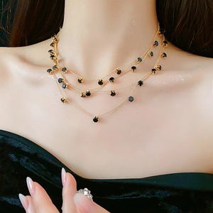 Gros plan d'un collier doré multicouche orné de pendentifs en zircon noir de forme ronde