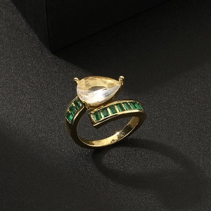 Close-up of gold ring featuring pear-cut clear stone and emerald green side stones