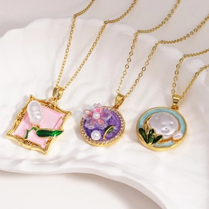 Three elegant gold necklaces with floral enamel pendants and pearls on a white shell tray