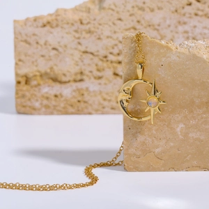 Detailaufnahme eines goldfarbenen Mond-Stern-Anhängers mit Opal auf Naturstein