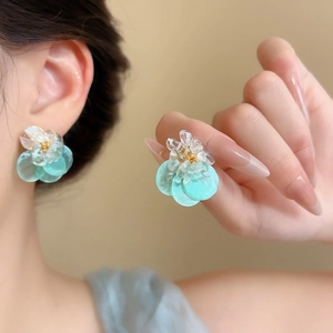 Close-up detail of stylish teal shell flower stud earrings worn on ear and held in hand