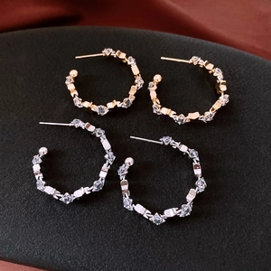 Detail of C-shaped hoop earrings in gold and silver finish with inlaid cubic zirconia stones