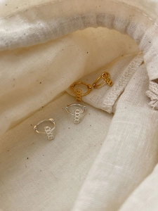 Detail of gold and silver GOOD letter hoop earrings resting on a beige canvas pouch