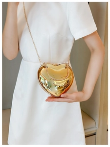 Golden heart-shaped acrylic evening bag with metallic chain strap shown by a model