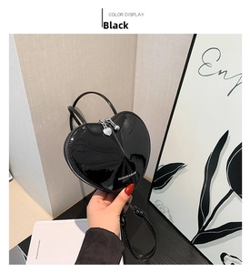 Detail einer schwarzen herzförmigen Handtasche aus Lackleder mit silbernen Herz-Reißverschluss-Anhängern