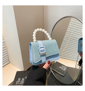 Close-up of light blue mini bag with glitter flap, pearl handle and gold chain strap