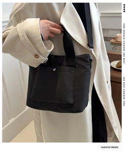 Detalle del bolso de nailon negro con bolsillo frontal y botón de presión de metal plateado