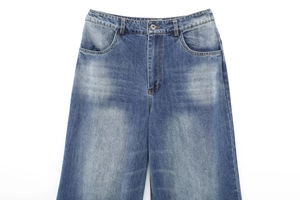 Detailed close-up of washed blue denim jeans waist, pocket, and fly stitching details
