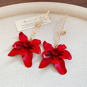 Macro detail of red orchid drop earrings with gold metal leaves on a textured tray