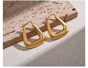 Macro shot of minimalist gold brushed metal U-shape geometric hoop earrings on stone