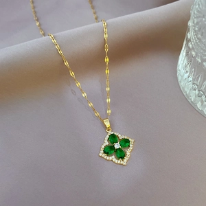 Macro detail of gold four-leaf clover pendant with green gemstone and micro zircon inlays