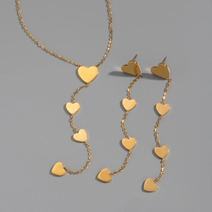 Close-up of a polished gold stainless steel jewelry set with heart pendants and tassel