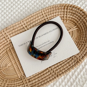 Close-up of amber tortoiseshell acetate hair tie with gold label on white card and rattan tray