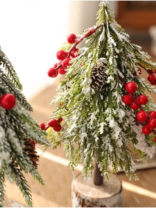 Close-up of mini snow-covered Christmas tree with red berries and pine cones on wood base