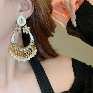 Macro view of ethnic gold teardrop earrings with white pearls and tassels on a model