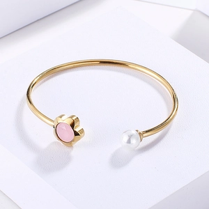 Detail of gold open cuff bracelet featuring a pink flower stone and white pearl